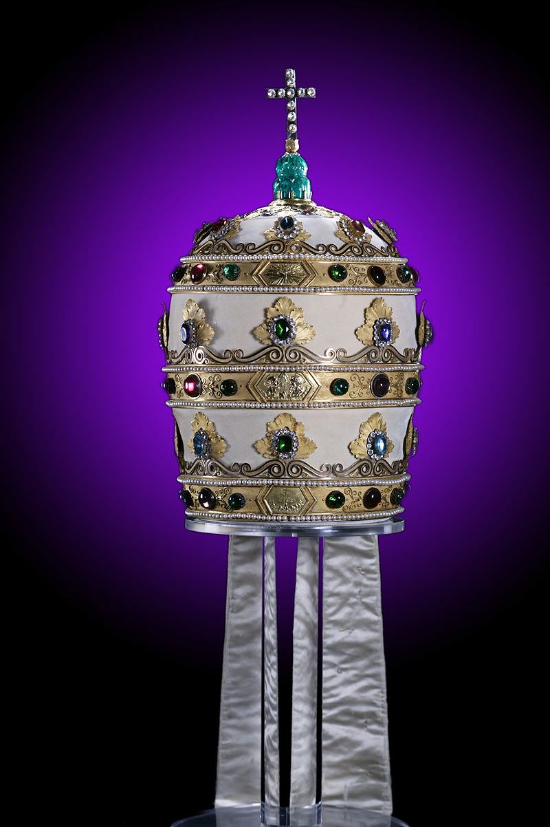 上图:拿破仑三重冕(Napoleon Tiara),是拿破仑于1805年送给教宗庇护七世的三重冕(Triregnum),虽然用珠宝装饰得非常华丽,却故意做得又小又重,难以佩戴。每道箍的中间原来都有一个美化拿破仑的浮雕,后来被圣经经文所取代:上层是徒二十28,中间是启十一4,底层是诗八十五10。 教宗本笃十五世卖掉头饰的珠宝为一战受难者筹款,代之以玻璃复制品。